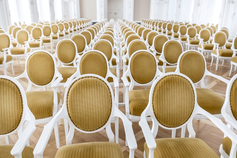 Platzhalter: Reihenbestuhlung mit hellen Polsterstühlen in einem großen Saal